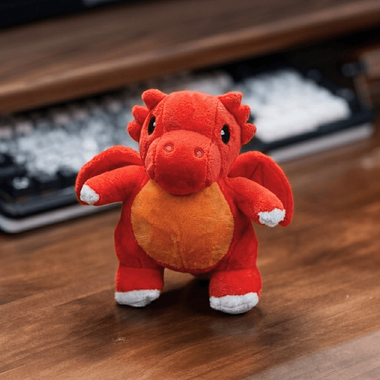 Red plush dragon toy on a wooden surface with a keyboard in the background