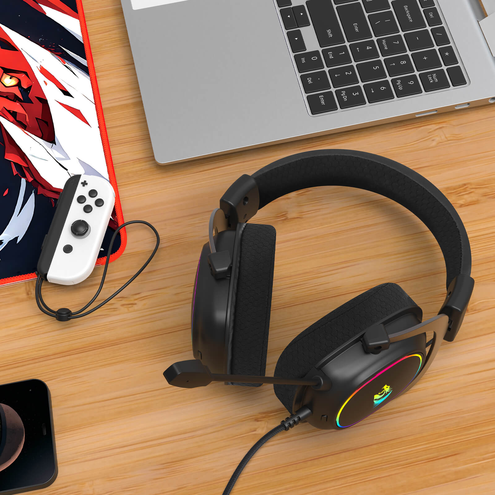 Gaming headset on a wooden desk with a laptop, Switch console, and controller.
