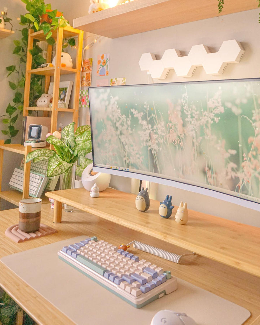 Neat desk setup with a curved monitor, pastel Redragon K673 PRO mechanical keyboard, Totoro figurines, and green plants.