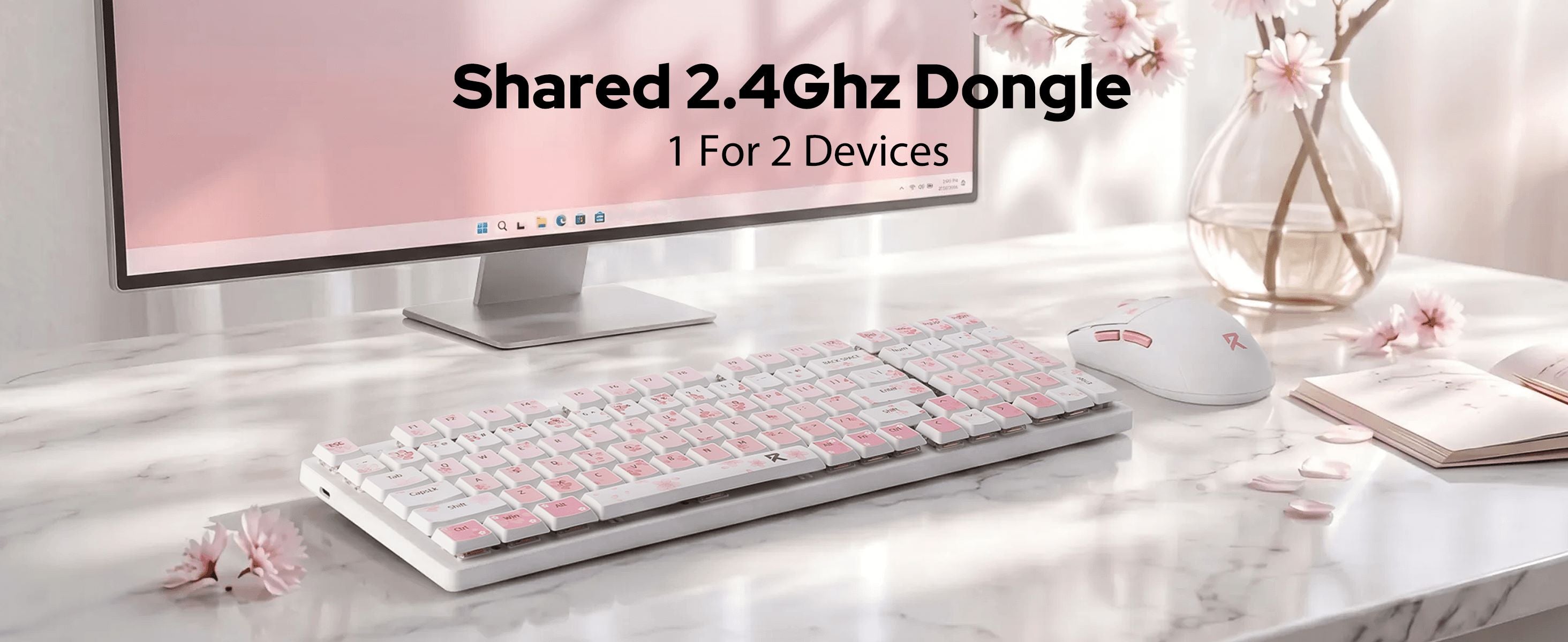 A white and pink wireless keyboard and matching mouse set on a marble desk in front of a computer monitor, with text overlay reading 'Shared 2.4Ghz Dongle 1 For 2 Devices'.