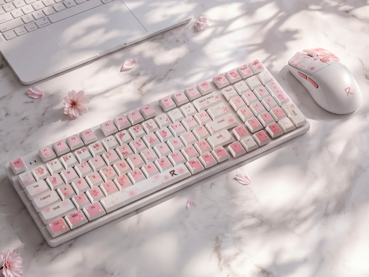A white mechanical keyboard and matching white computer mouse with pink cherry blossom patterns, arranged on a light marble desk with soft leaf shadows and scattered pink flower petals.