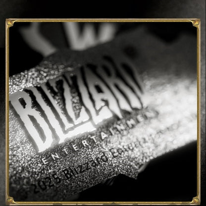 Within a gold-cornered frame, this black-and-white close-up shows a textured metallic emblem: bold "BLIZZARD" lettering glows under light, its grainy surface catching bright highlights against a softly blurred dark background.