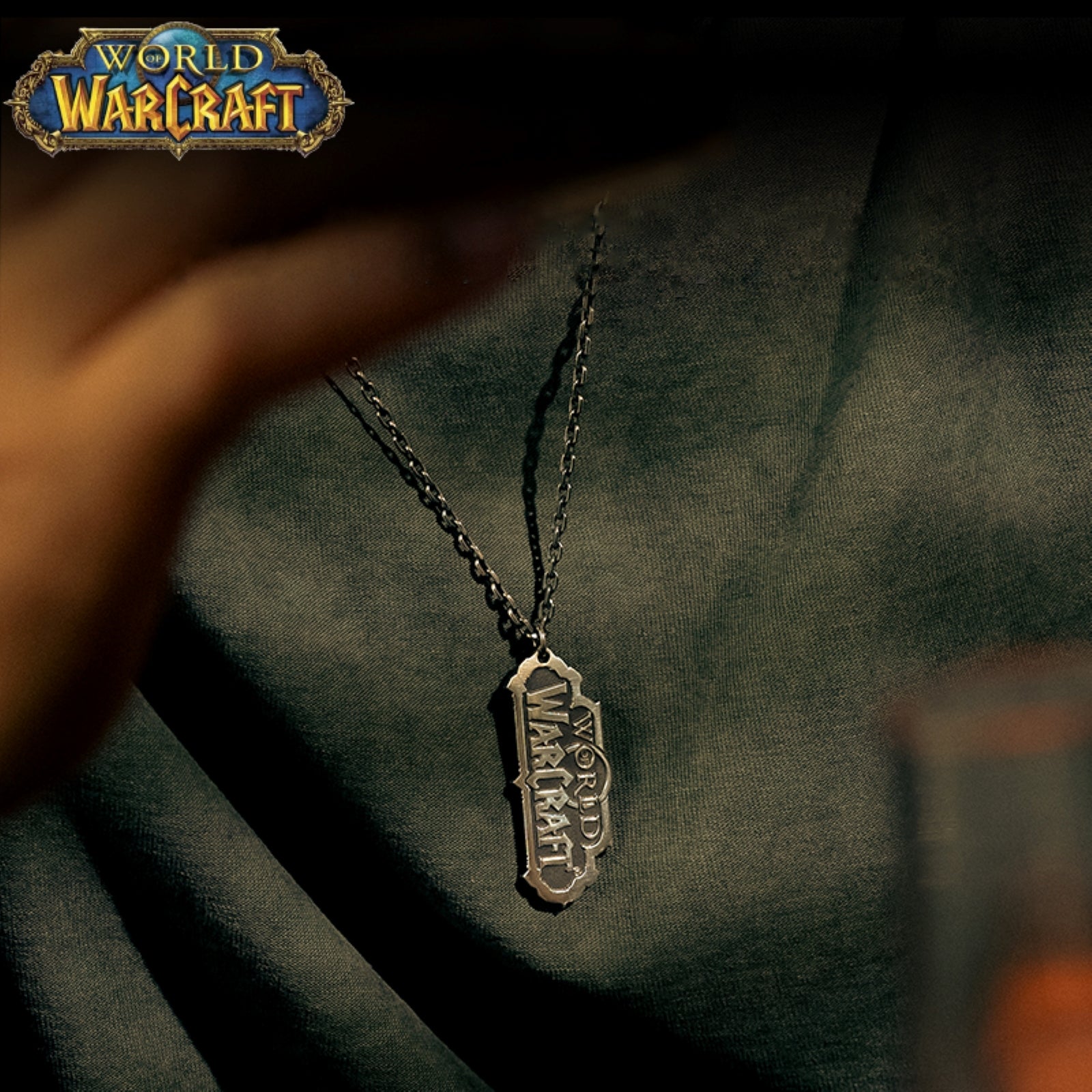 In the top corner sits the colorful "WORLD OF WARCRAFT" logo, while below, a metallic "WORLD OF WARCRAFT" pendant (on a chain) rests against dark fabric.