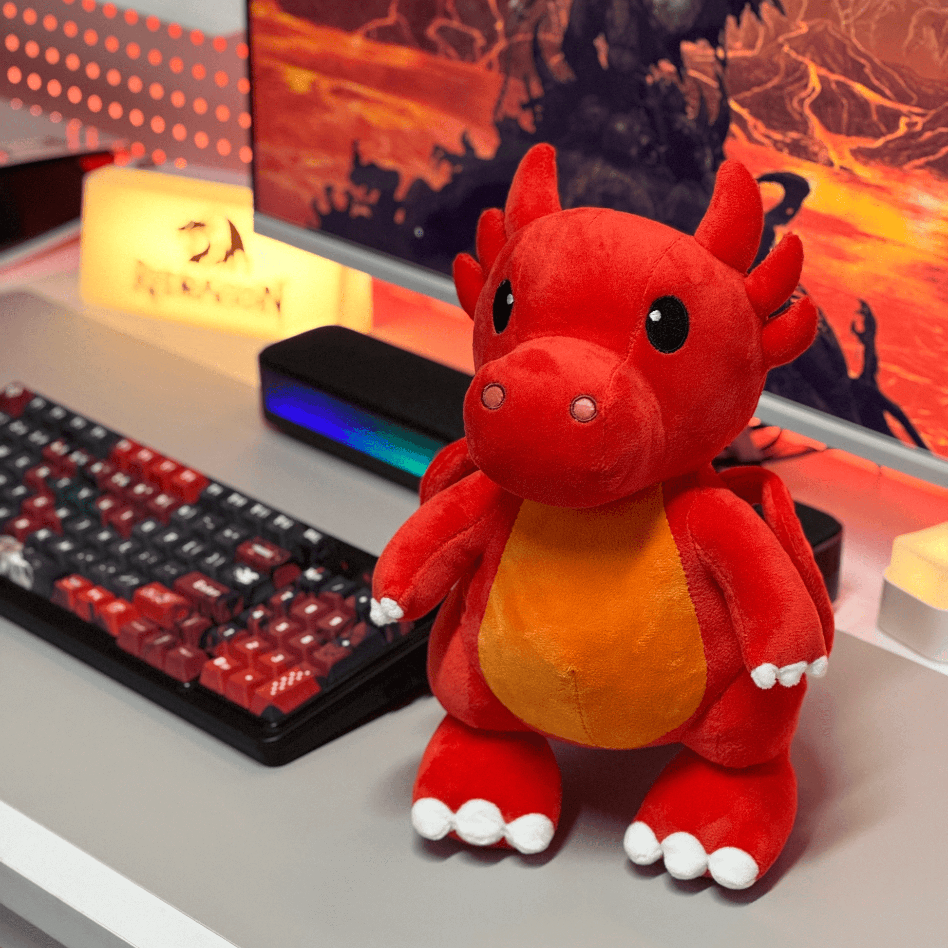 Red plush dragon toy on a desk with a computer setup in the background