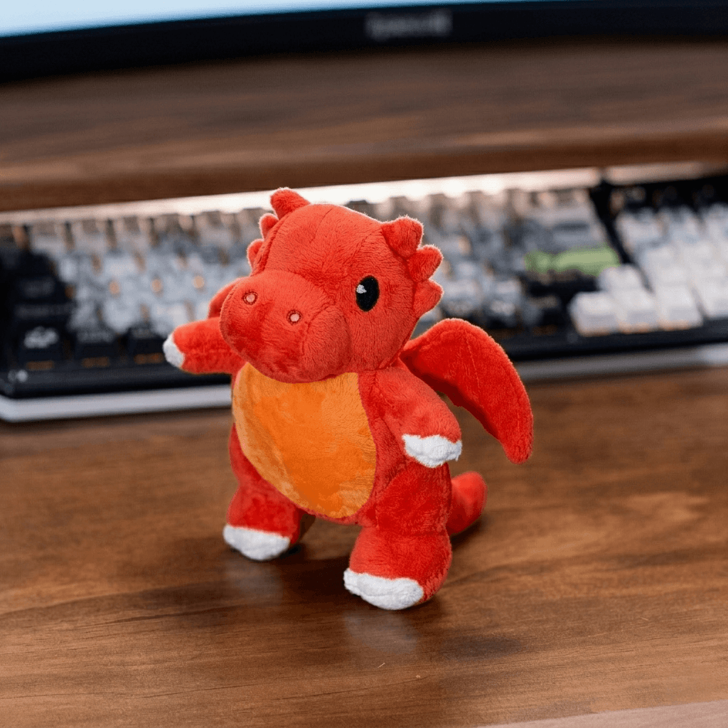 Red plush dragon toy on a wooden surface with a keyboard in the background