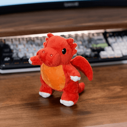 Red plush dragon toy on a wooden surface with a keyboard in the background