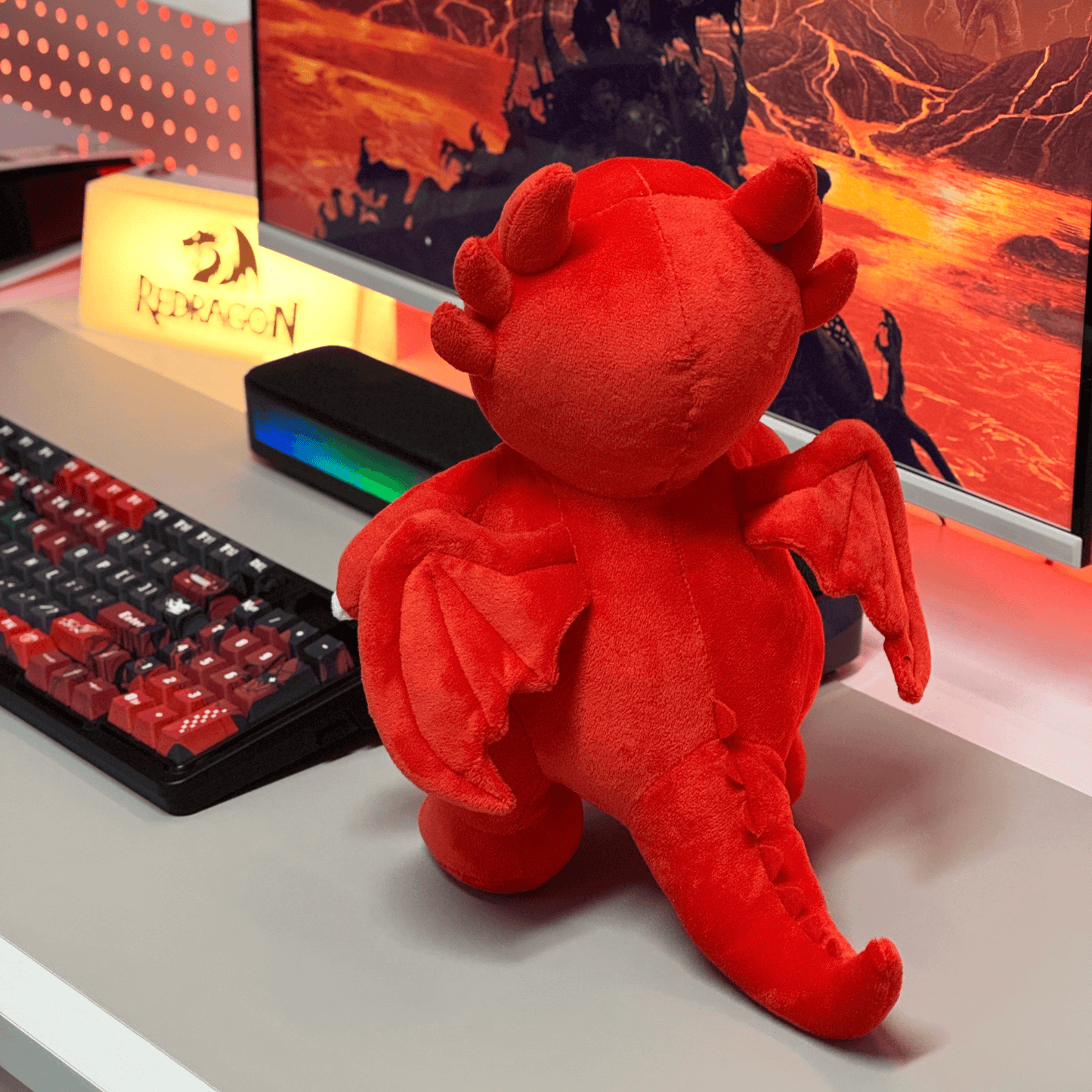 Red plush dragon toy on a desk with a computer setup in the background
