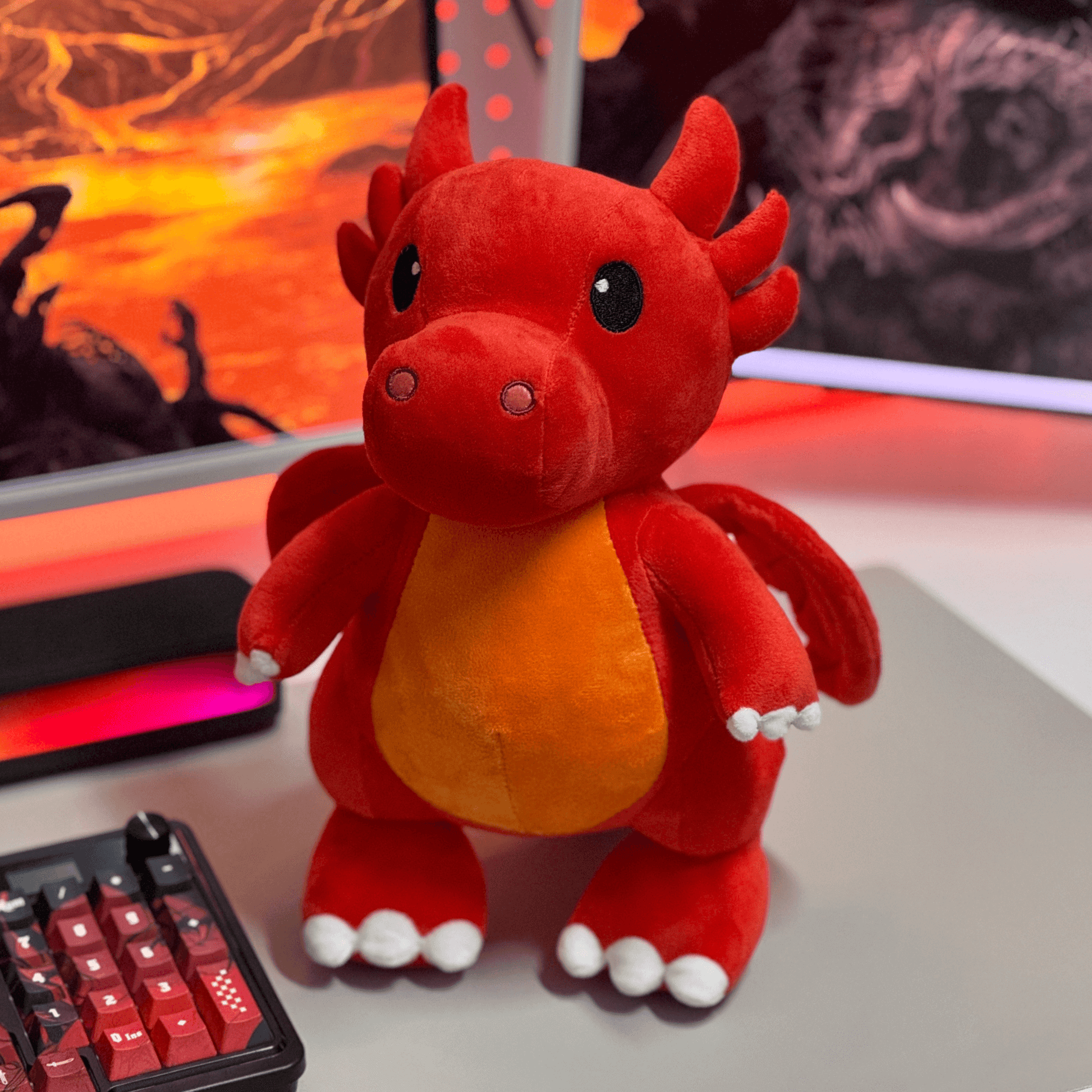 Red plush dragon toy on a desk with a computer setup in the background