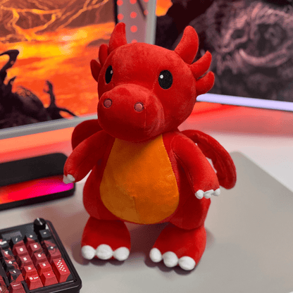 Red plush dragon toy on a desk with a computer setup in the background