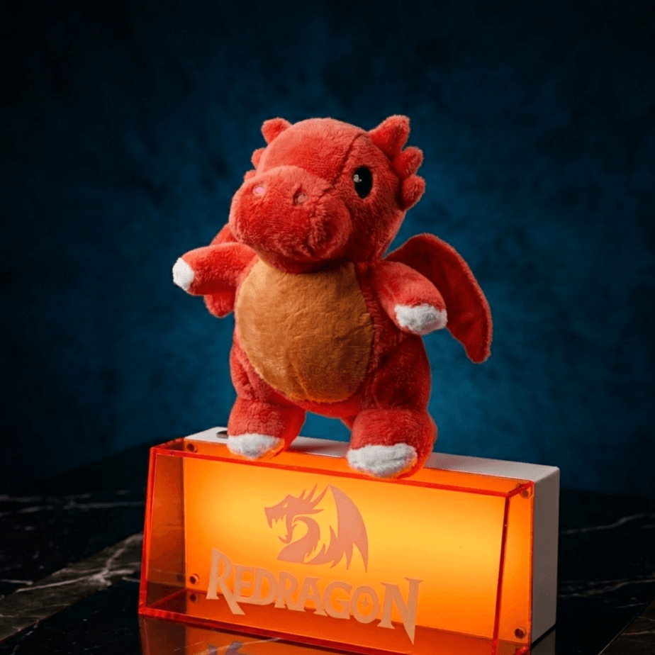 Red plush dragon toy on an orange stand with 'Redragon' logo against a dark background