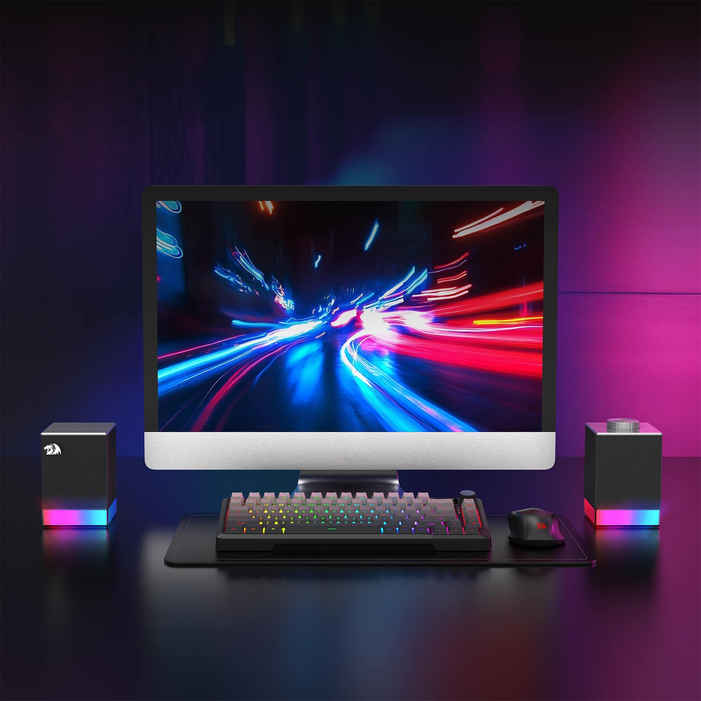 Gaming setup with monitor, keyboard, and speakers on a dark surface with colorful lighting.