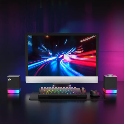 Gaming setup with monitor, keyboard, and speakers on a dark surface with colorful lighting.