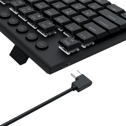 Close-up of a black mechanical keyboard showing the side profile, port buttons, and a black right-angle USB cable connected to a USB port on a black background.