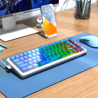 Colorful keyboard on a desk with a phone, mouse, and monitor in the background.