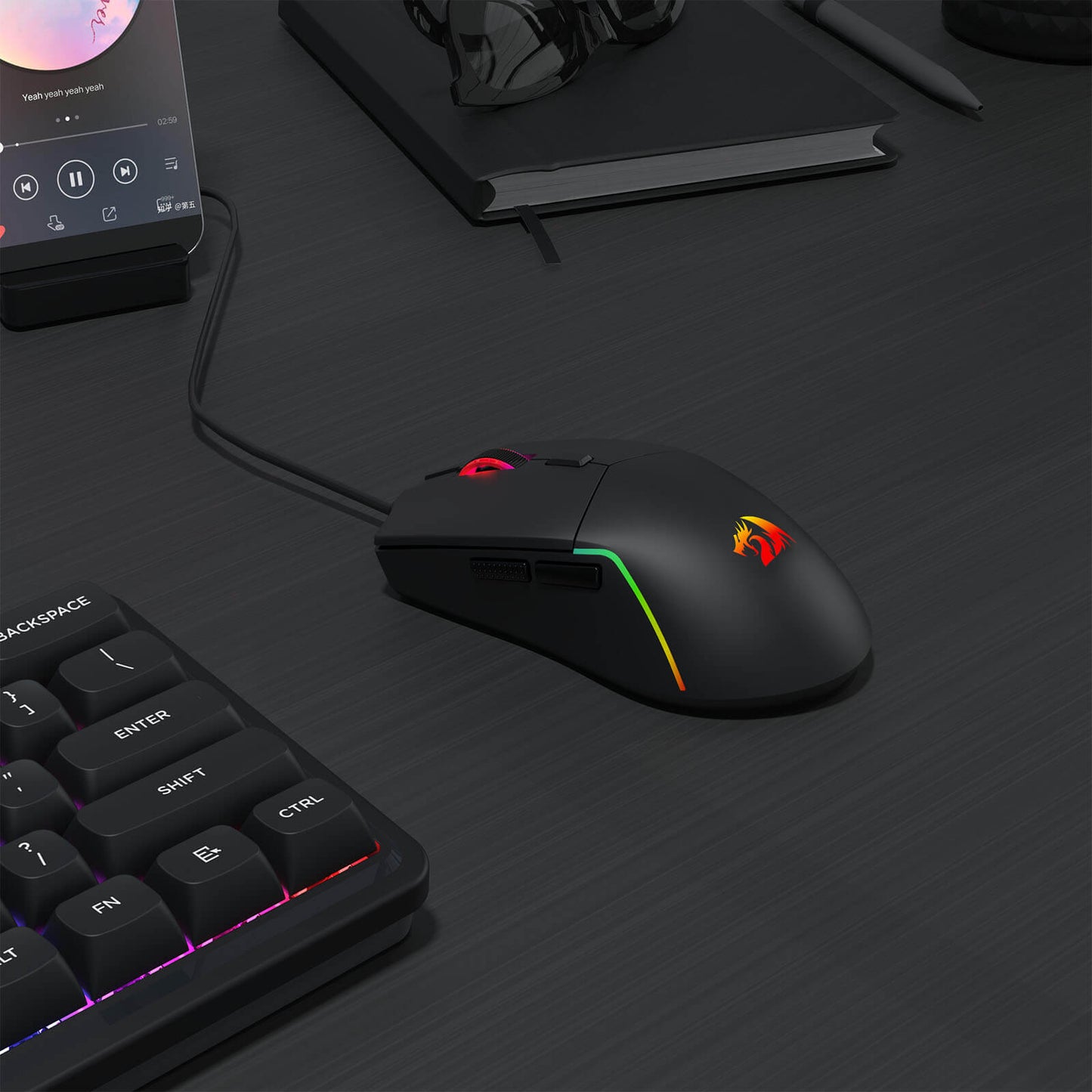 Redragon M730 Gaming mouse and keyboard on a dark surface with smartphone and notebook in the background