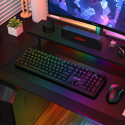 The Redragon RM104 Pro keyboard and RM104 mouse are displayed in a vibrant RGB-lit gaming setup, with a monitor, speakers, and a small potted plant.