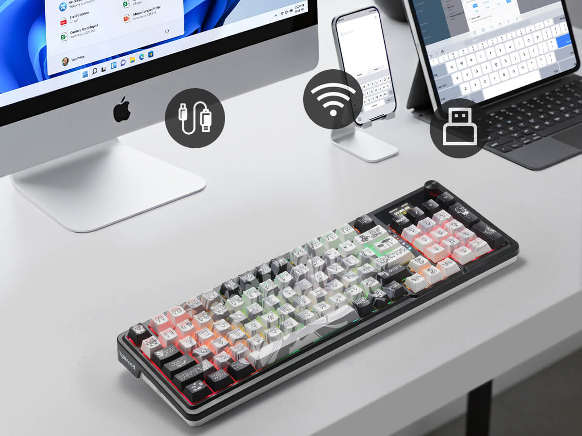 Keyboard with colorful keycaps on a desk with computer monitors and devices.
