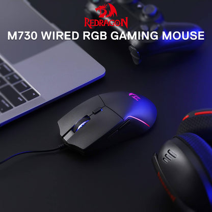 The Redragon M730 wired RGB gaming mouse is featured in a setup (with a laptop, controller, and headset), showcasing its sleek design and RGB lighting.