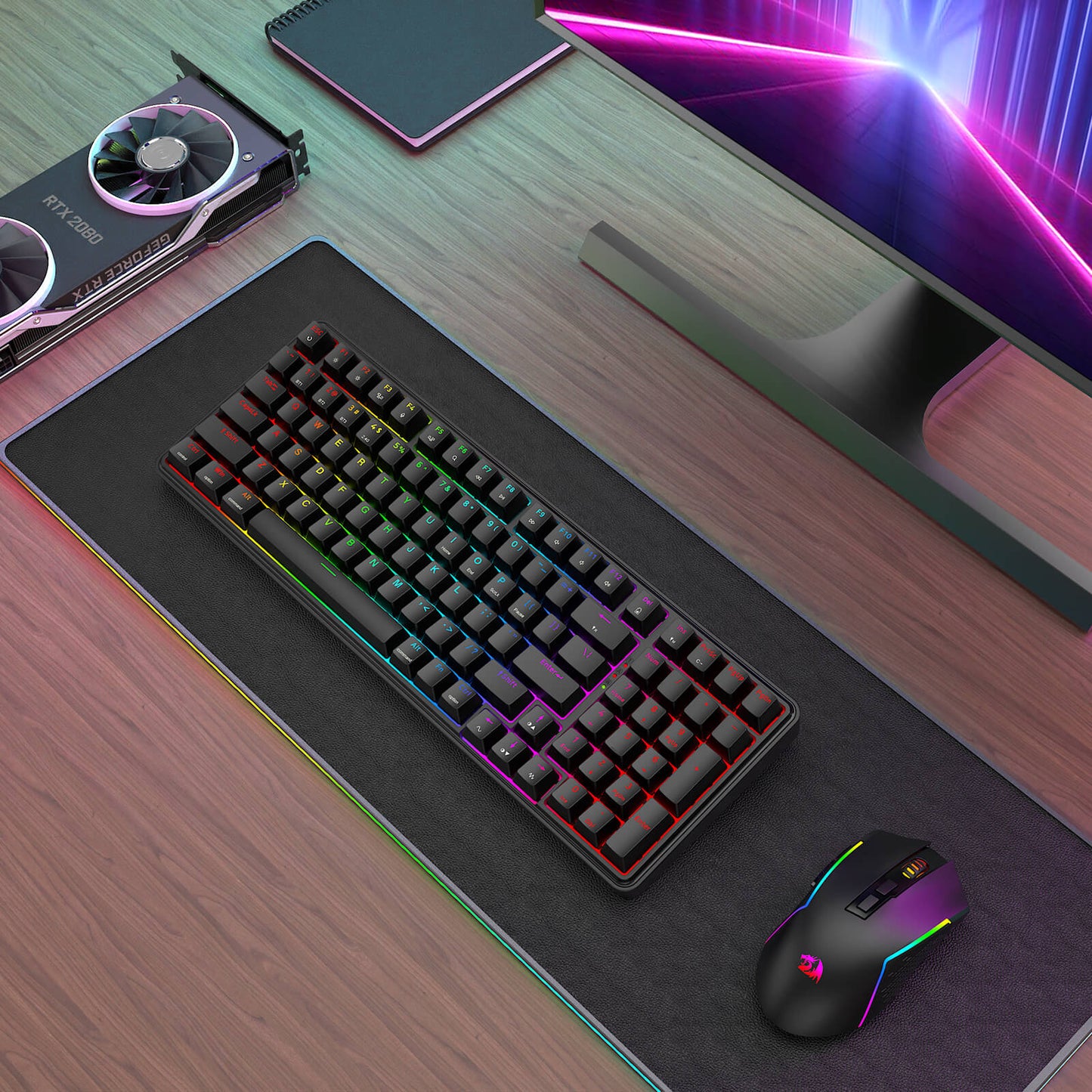The Redragon keyboard and mouse combo is displayed on an RGB desk mat in a gaming setup, alongside an RTX 2080 GPU and a monitor with neon lighting.
